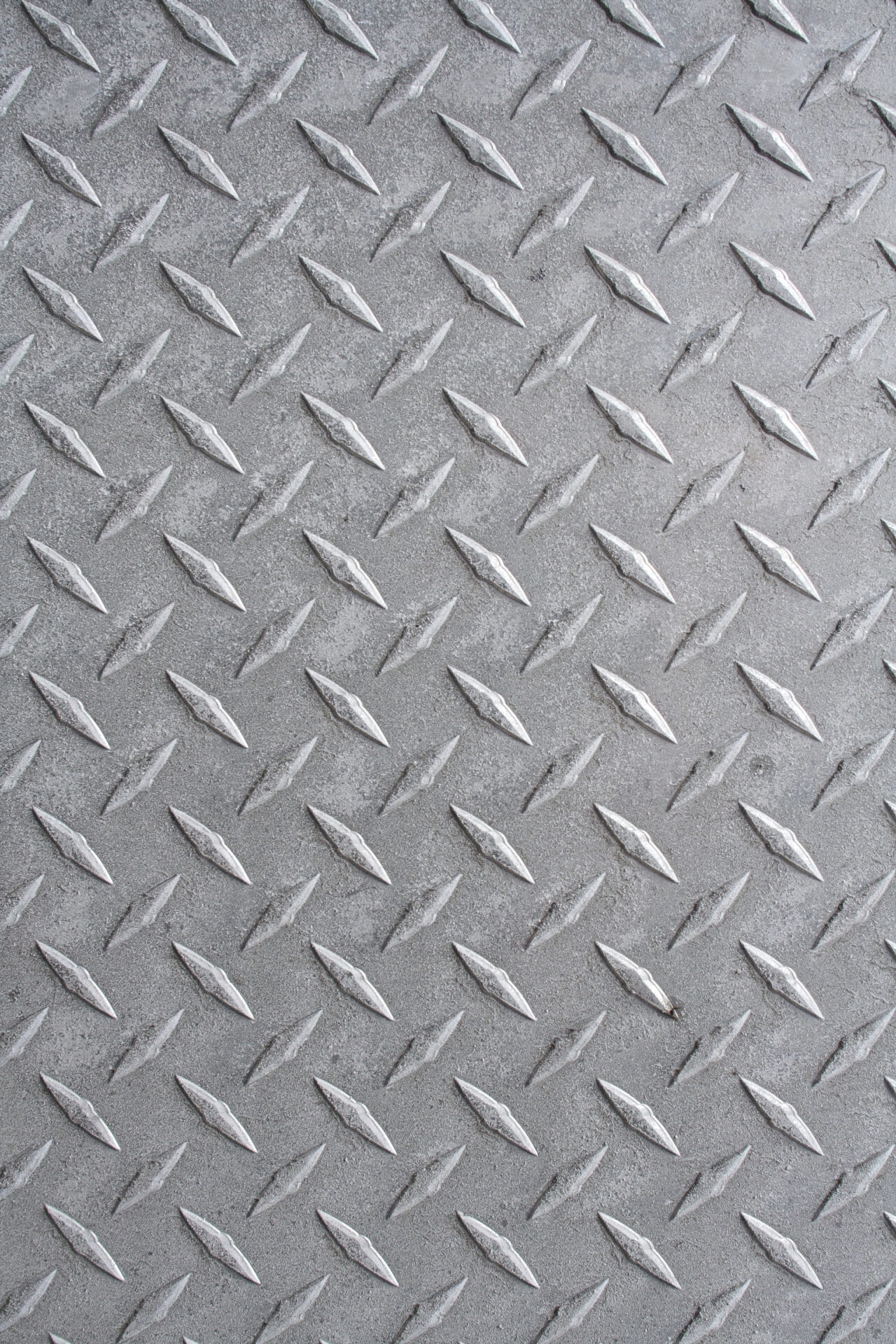 Close-up of textured metal surface featuring a diamond plate pattern, commonly used for industrial flooring and surfaces to prevent slipping. No people visible.