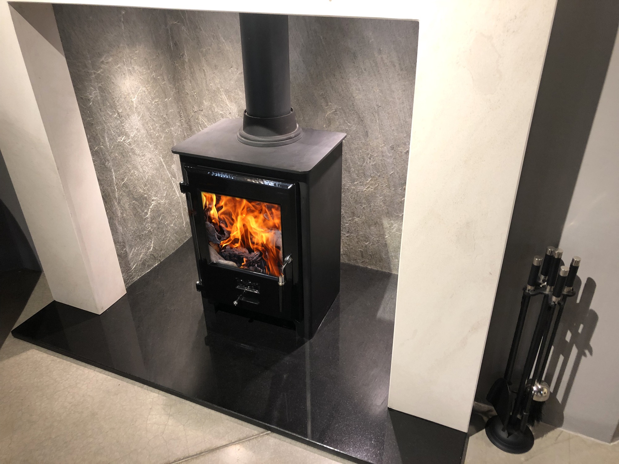 A cozy black wood-burning stove set against a grey stone backdrop, with visible flames and nearby fireplace tools, provides a warm ambiance.
