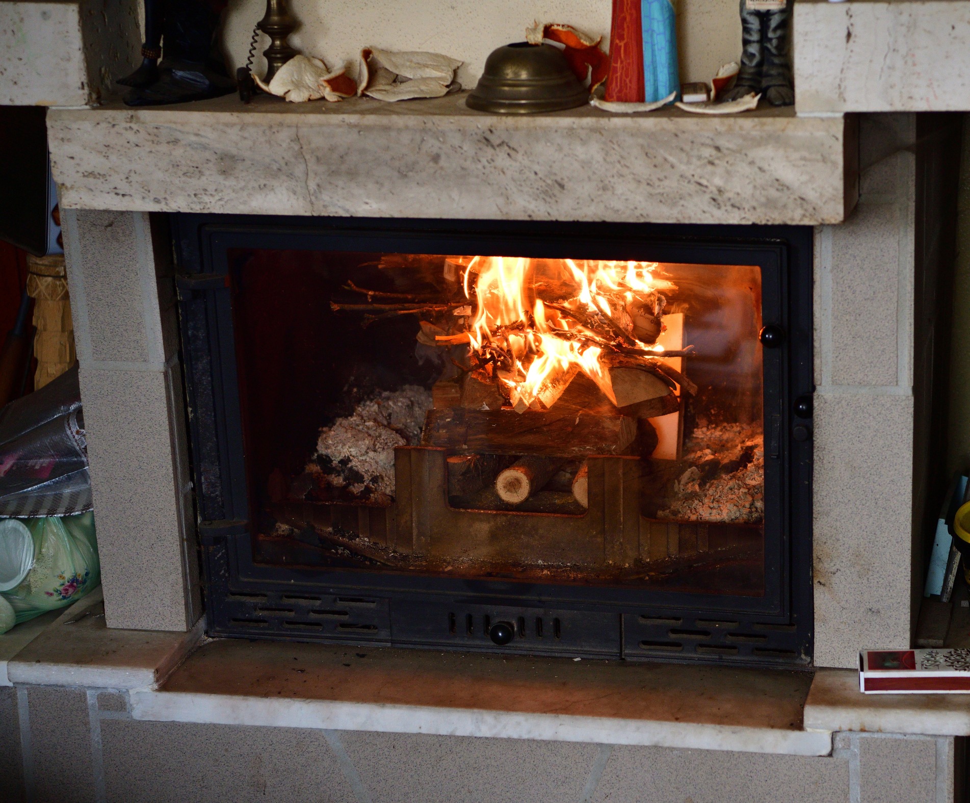 A cozy indoor scene featuring a lit fireplace with burning logs, surrounded by various decorative items and a marble mantle.