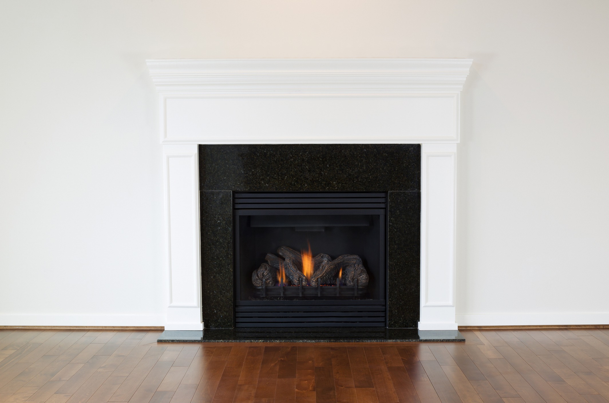 A classic white mantel surrounds a lit fireplace on a polished wooden floor, creating a warm, inviting indoor space.