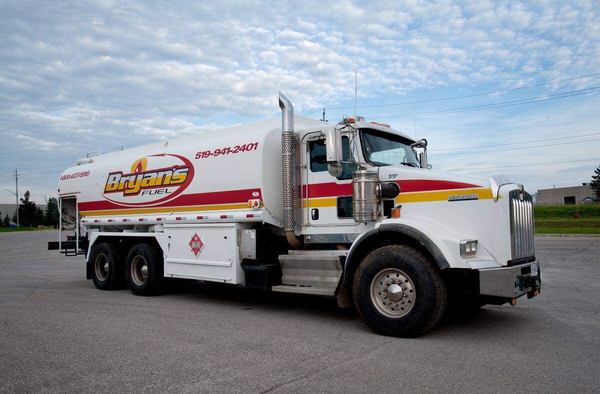 A large fuel delivery truck labeled "Bryan's Fuel" is parked on a paved lot under a partly cloudy sky. Road and buildings visible.