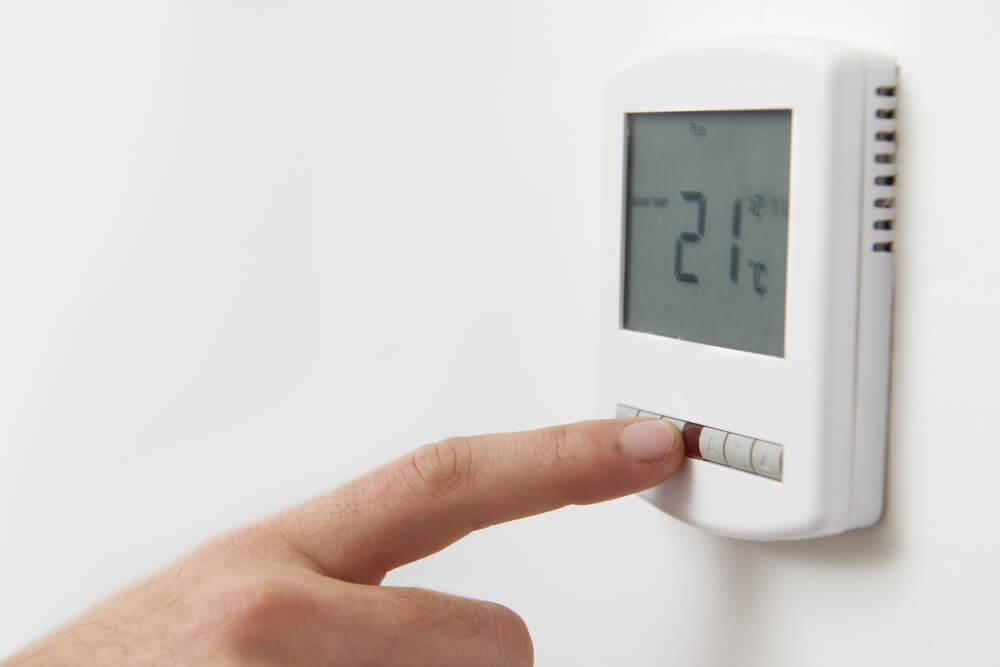 A person adjusts a digital thermostat mounted on a white wall, setting the temperature to 21°C for a comfortable indoor climate.