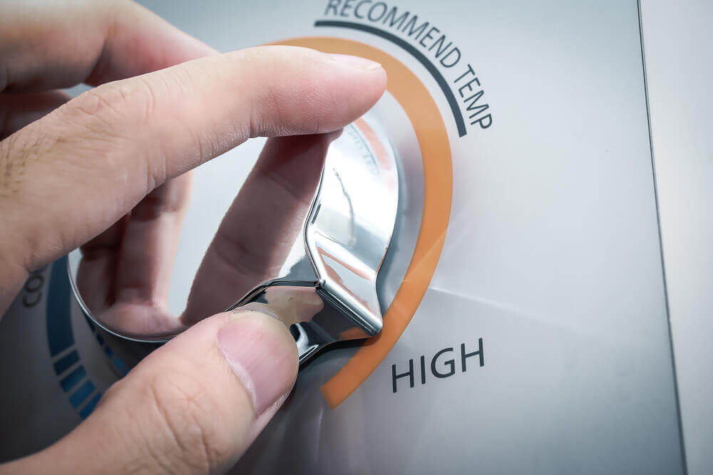 Close-up of a person's hand adjusting a silver knob on a temperature control panel, set towards the high setting.
