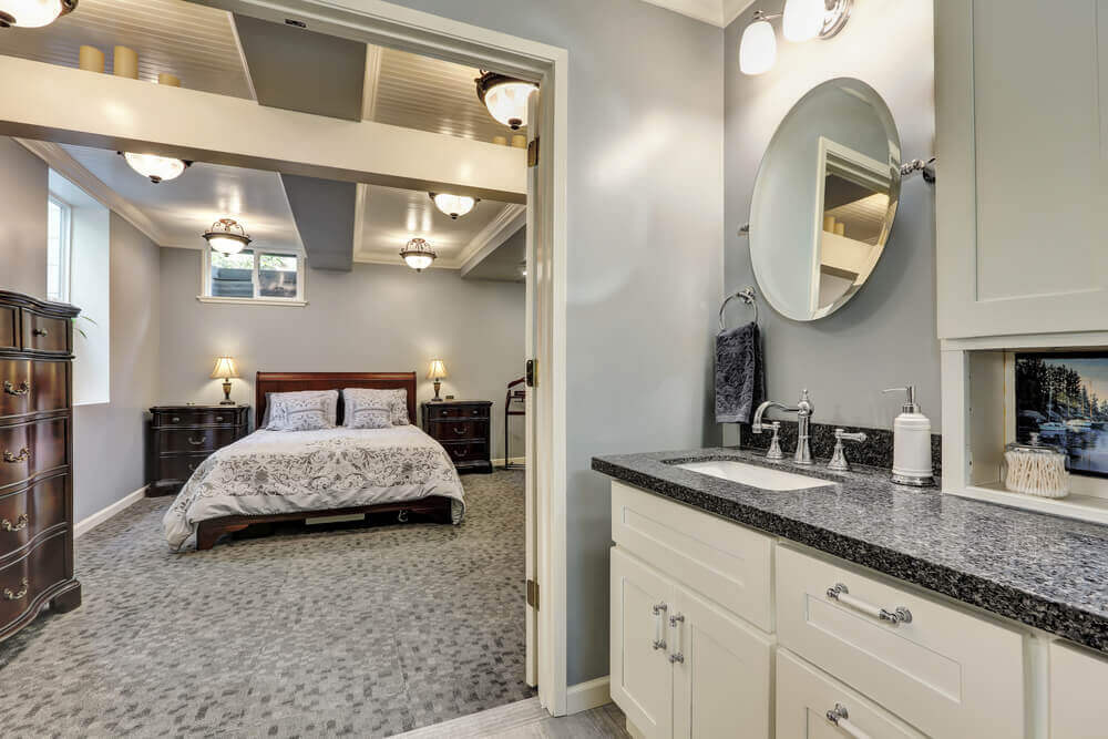 Spacious bedroom with elegant decor, attached bathroom featuring granite countertops and oval mirror. Soft lighting creates a cozy, inviting atmosphere.