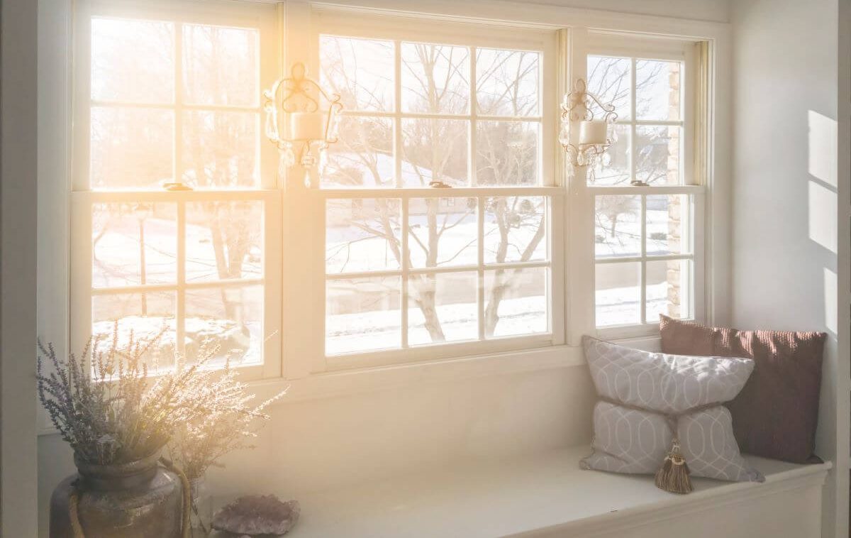 Sunlit cozy window seat with decorative pillows, vase of flowers, and soft sunlight streaming through paned glass, creating a warm, inviting atmosphere.