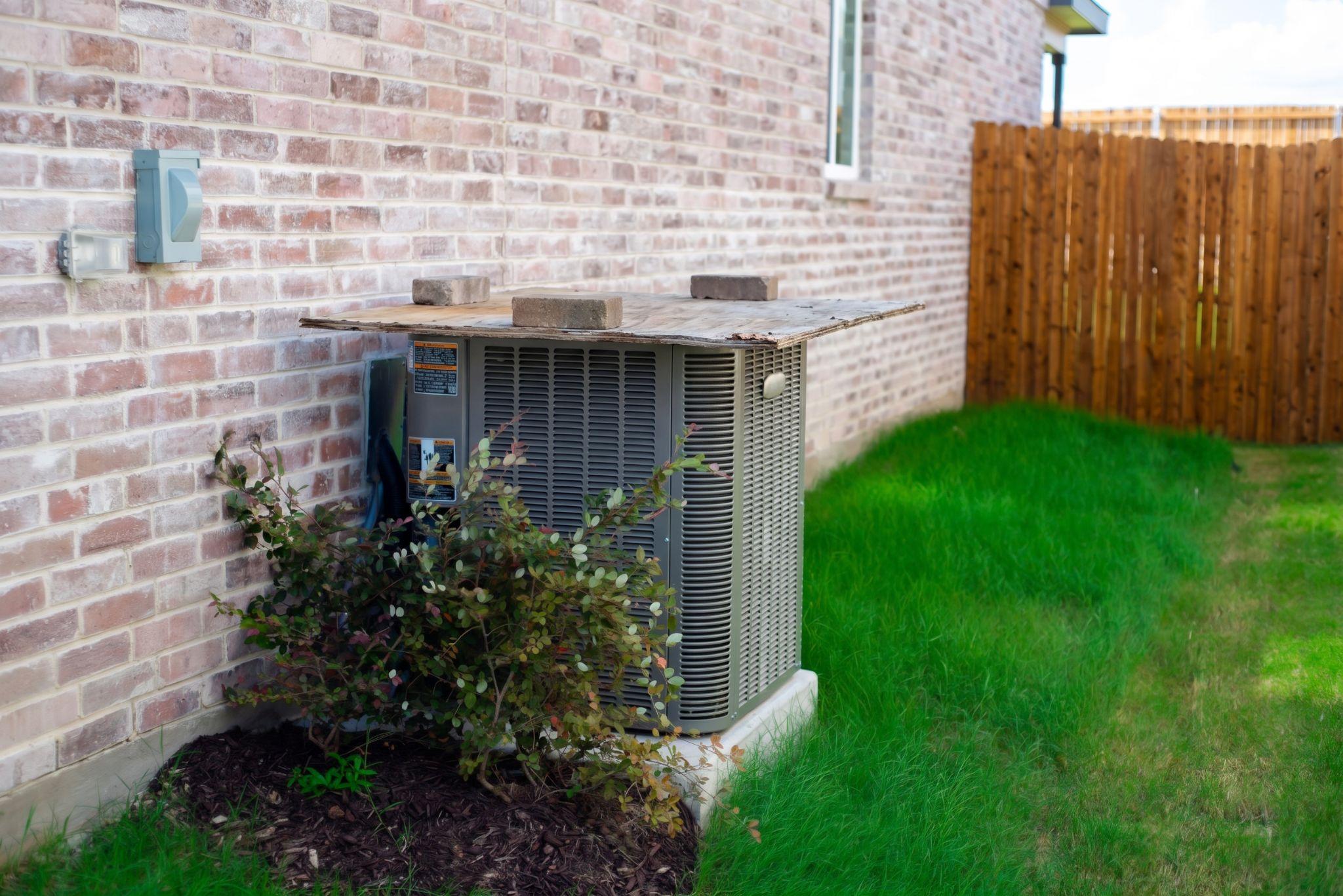 Air conditioner unit with plywood on top and bricks.