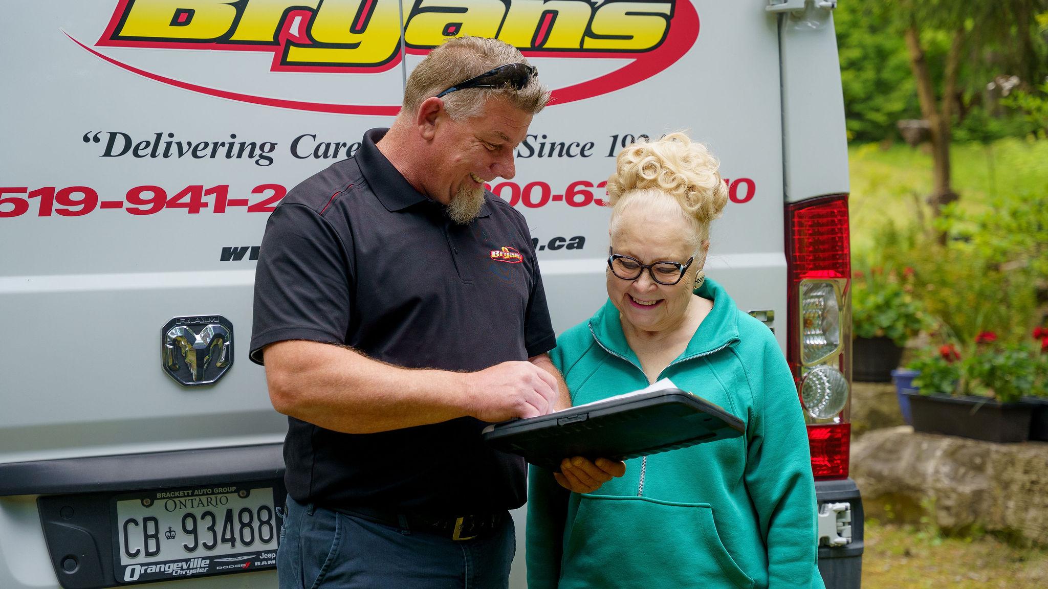 Bryan's Fuel technician and woman smiling looking at papers in front of work truck.