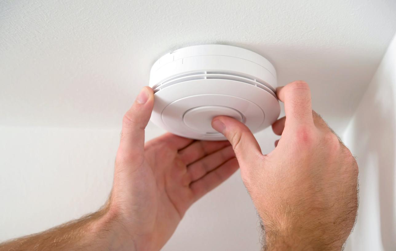 Hands changing a smoke detector battery.