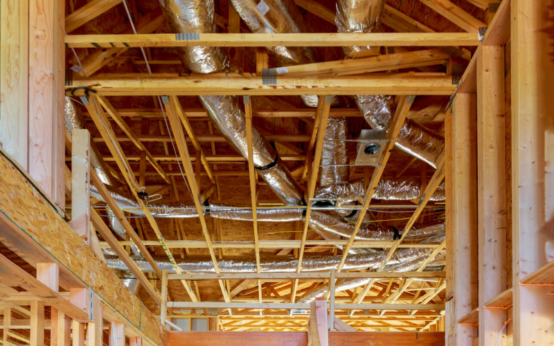 The image shows an unfinished building interior with exposed wooden beams, insulation wrapped in reflective foil, and ductwork running across the ceiling structure.
