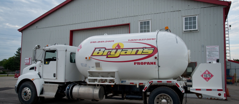 A white propane delivery truck is parked near a red and gray industrial building, with the company's name, "Bryan's," prominently displayed on the tank.