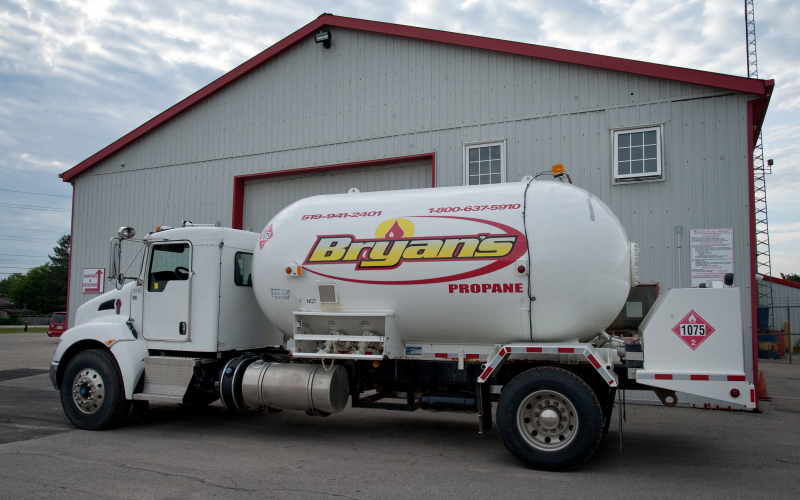 A white propane delivery truck is parked near a red and gray industrial building, with the company's name, "Bryan's," prominently displayed on the tank.